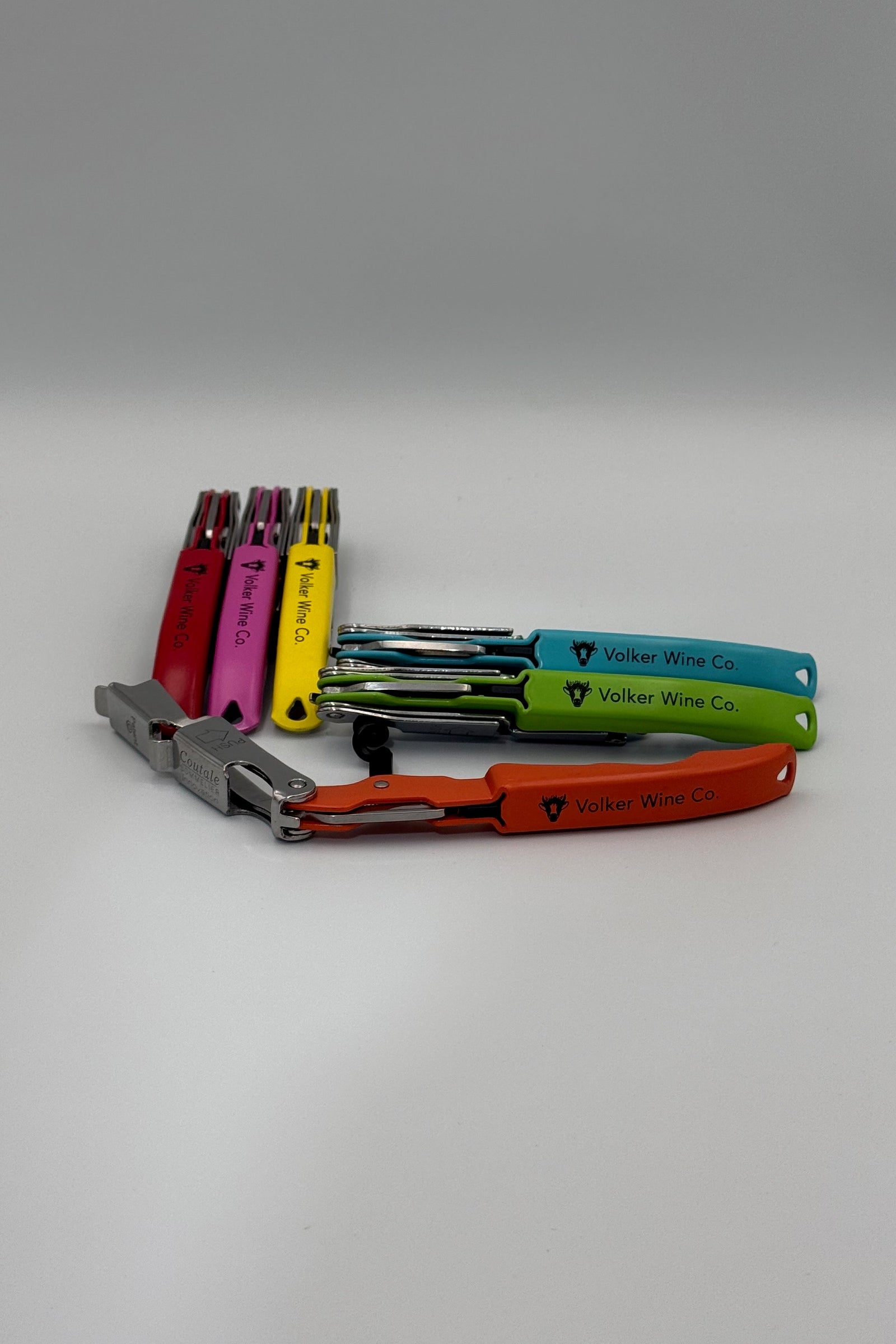 A set of multi-tool wine bottle openers in various colors including orange, green, blue, yellow, and pink, with one silver tool in the foreground. The tools are branded with 'Volker Wine Co.
